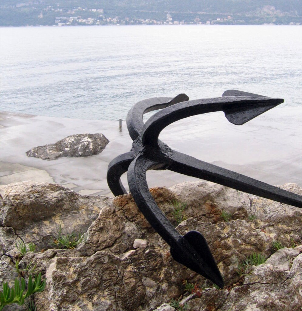 Uma âncora de ferro epoiada sobre vegetação marinha numa praia.