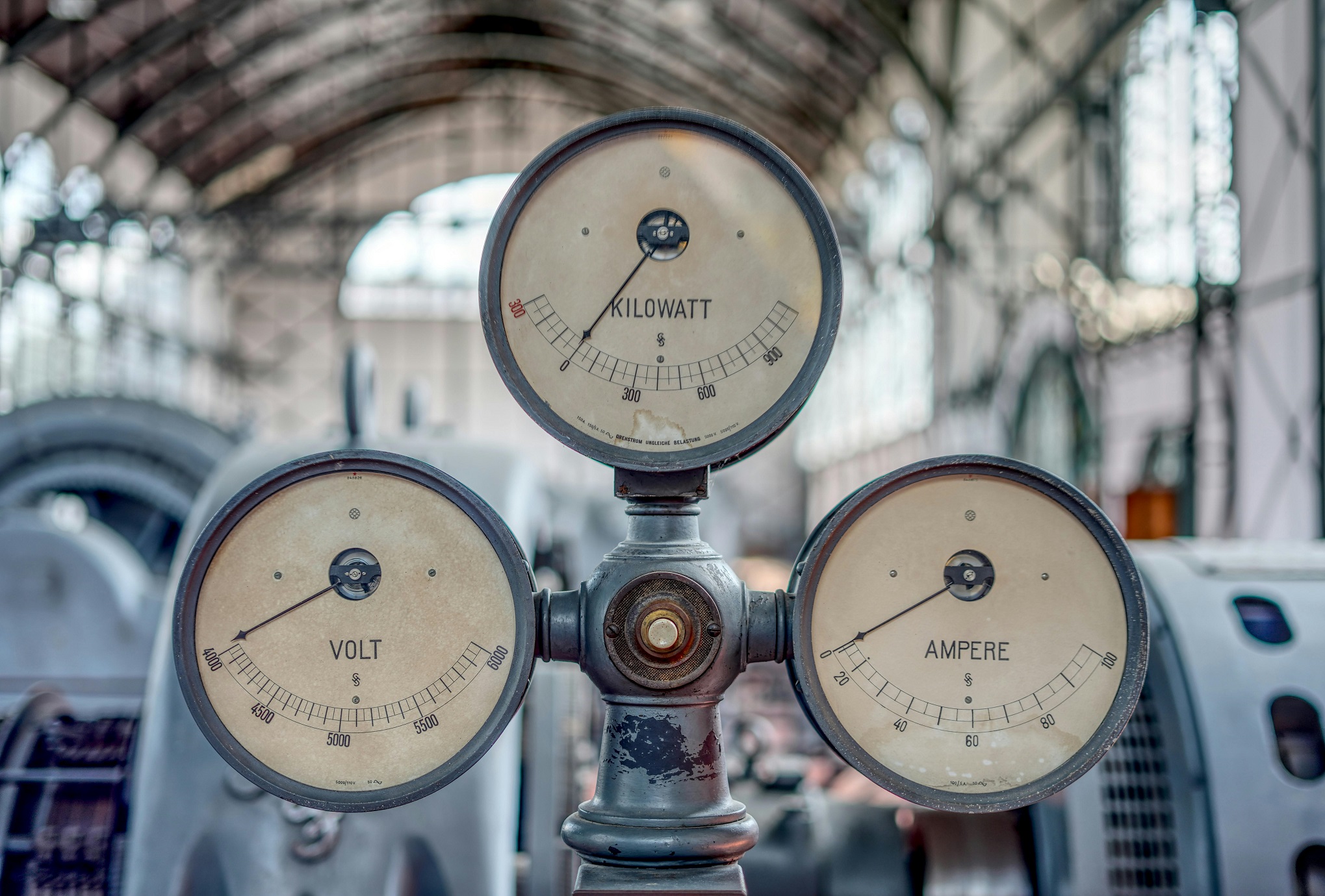 Instrumento de medição de uma fábrica, com três mostradores redondos, de ponteiros, medindo Volts, Kilowatts e Amperes.