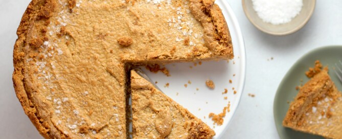 Foto de uma torta vista de cima, com uma espátula retirando um pedaço. Ao lado da torta, um prato menor já com um pedaço dela.