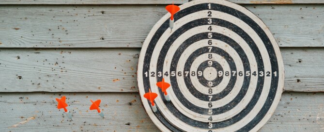 Foto de um alvo em que os dardos estão concentrados à esquerda do centro, além de dois deles estarem fora do próprio alvo.