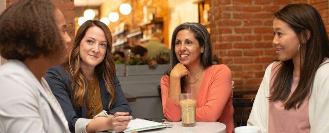Quatro mulheres sentadas em volta de uma mesa conversando de maneira descontraída.