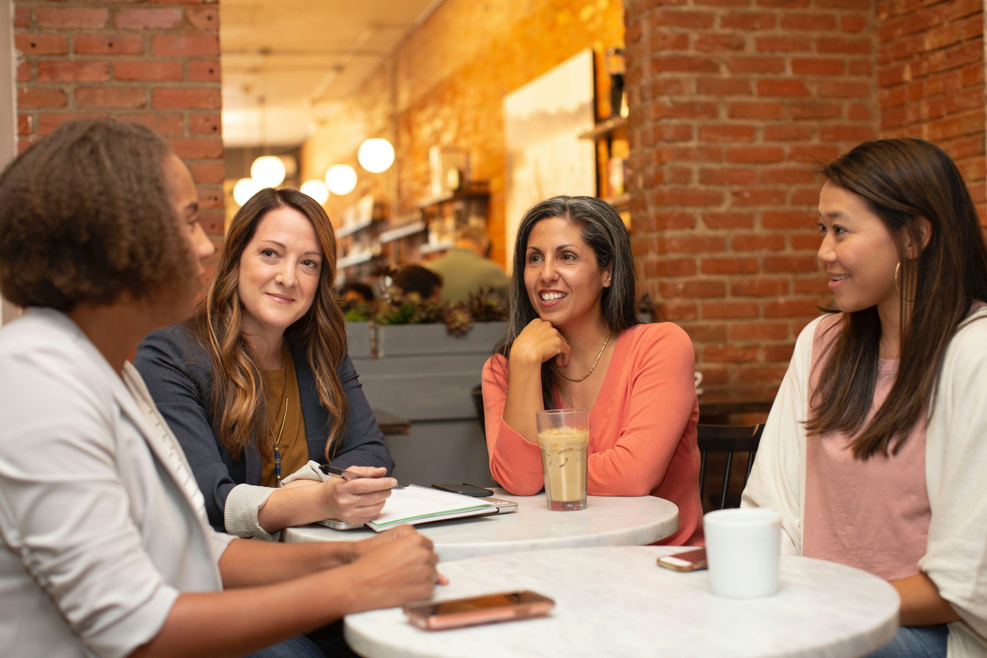 Quatro mulheres sentadas em volta de uma mesa conversando de maneira descontraída.