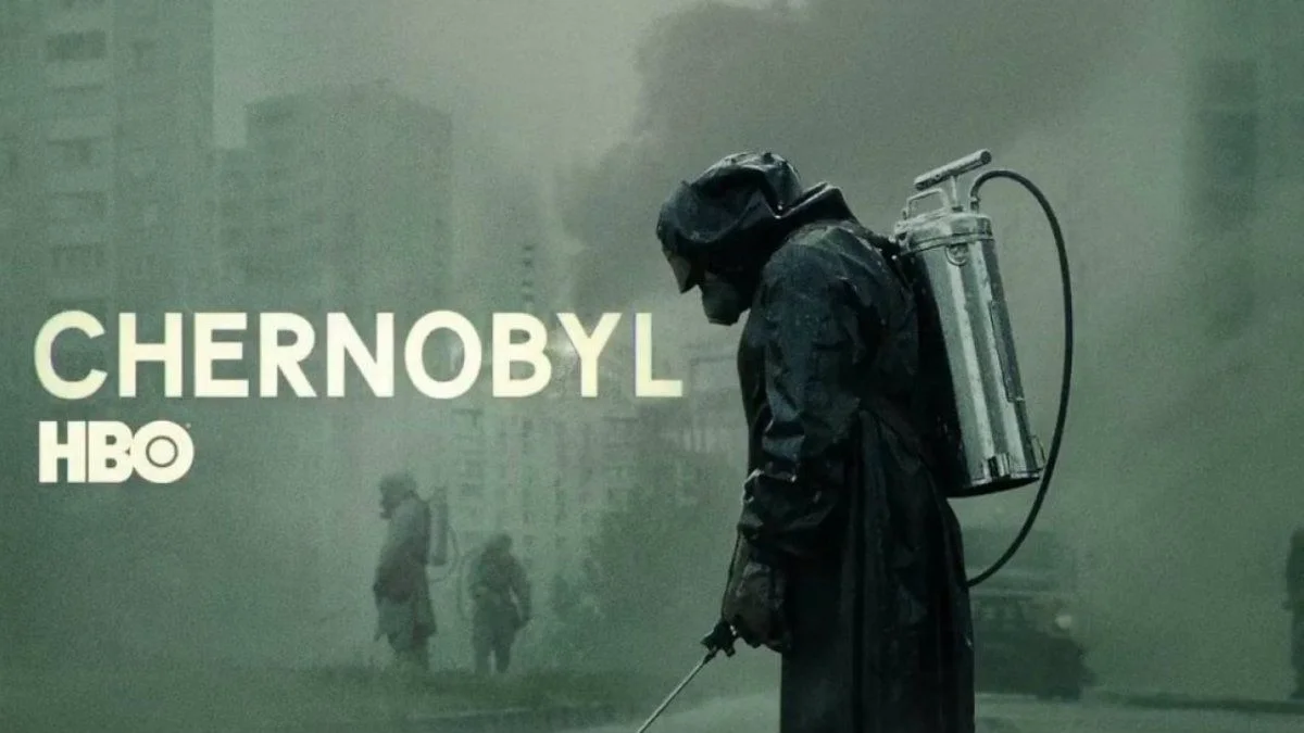Foto promocional da minissérie Chernobyl, da HBO. A imagem mostra uma pessoa com uma roupa protetora contra radiação, num tecido bem grosso de cor cobre, óculos de proteção e máscara anti-gases. Ela tem um olhar assustado e olha diretamente para a câmera.