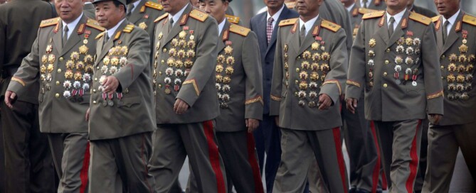 Um grupo de militares norte coreanos portando uma quantidade excessiva de medalhas que cobre quase toda a parte frontal dos seus uniformes.