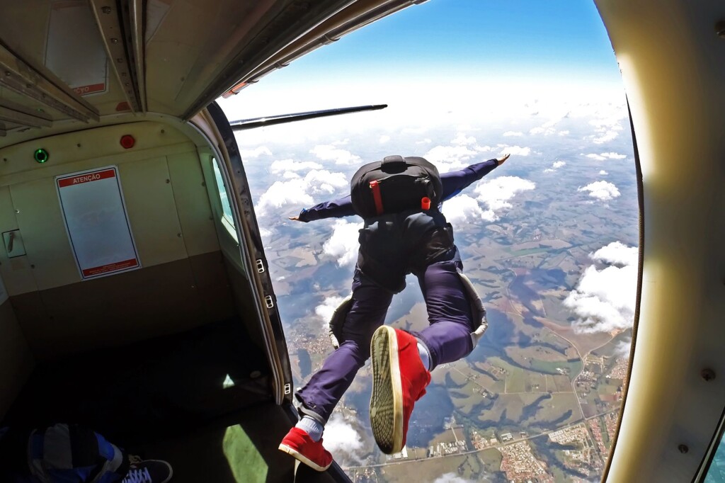 Imagem de dentro de um avião em pleno voo, com um paraquedista saltando da porta.
